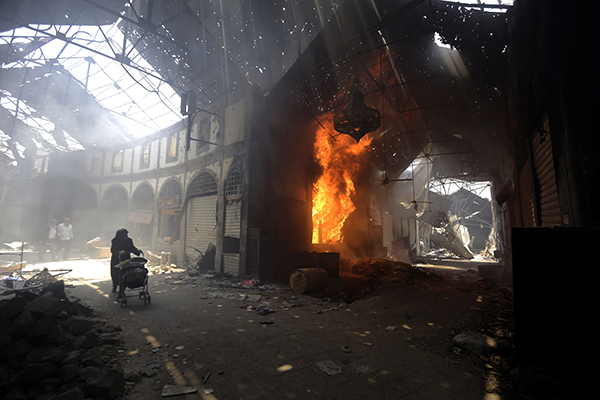 SYRIA, HOMS : A woman walks past a burning shop in the Maskuf market in the Old City of Homs, some 162 kilometres north of the capital Damascus, on May 12, 2014.