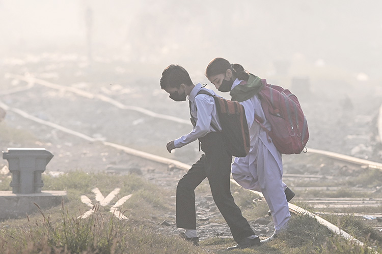Schoolchildren wearing masks walk across a railway track amid thick smog in Lahore, Pakistan, on 20 November 2024. © Arif Ali / AFP