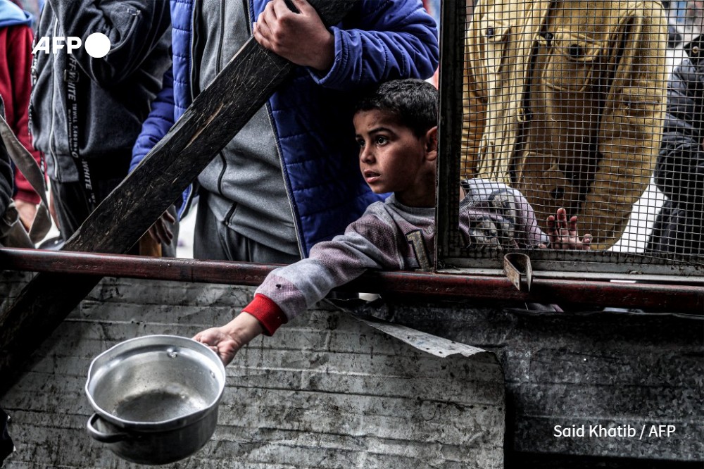 A boy holds out an empty pot as he waits with other displaced Palestinians queueing for meals