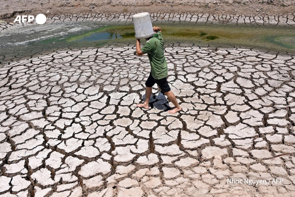 A man carries a plastic bucket across the cracked bed of a dried-up pond in Vietnam's southern Ben Tre province