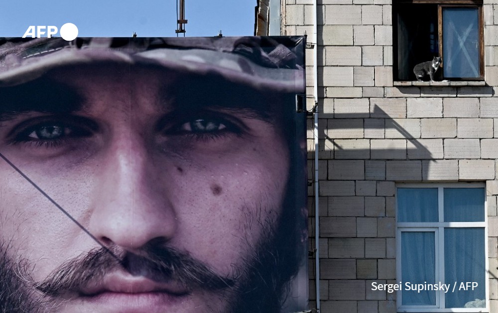 A cat looks out from a window of a residential building with a huge recruiting placard of Ukraine's Azov Brigade 