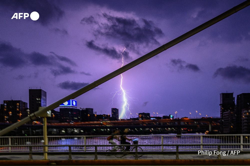 People ride bikes on the Shin-Ohashi Bridge as a bolt of lightning strikes the sky above the Tokyo