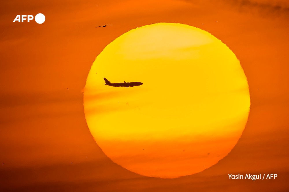 A passenger aircraft is silhouetted by the setting sun in the Eminonu district of Istanbul
