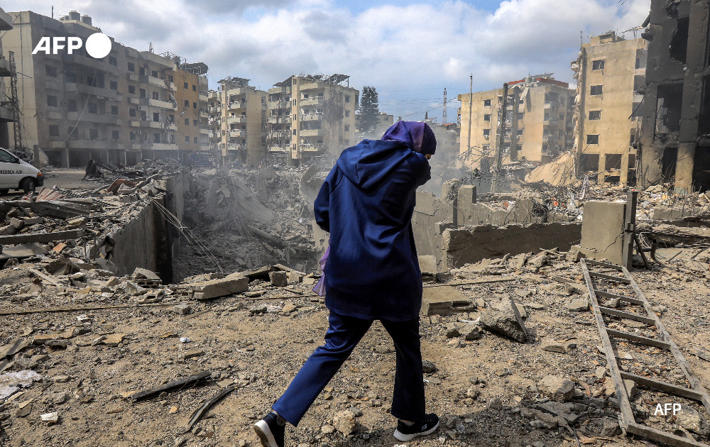 A woman walks past a crater where a collapsed building stood following an overnight Israeli air strike on the neighbourhood of Kafaat in Beirut's southern suburbs, on October 7, 2024