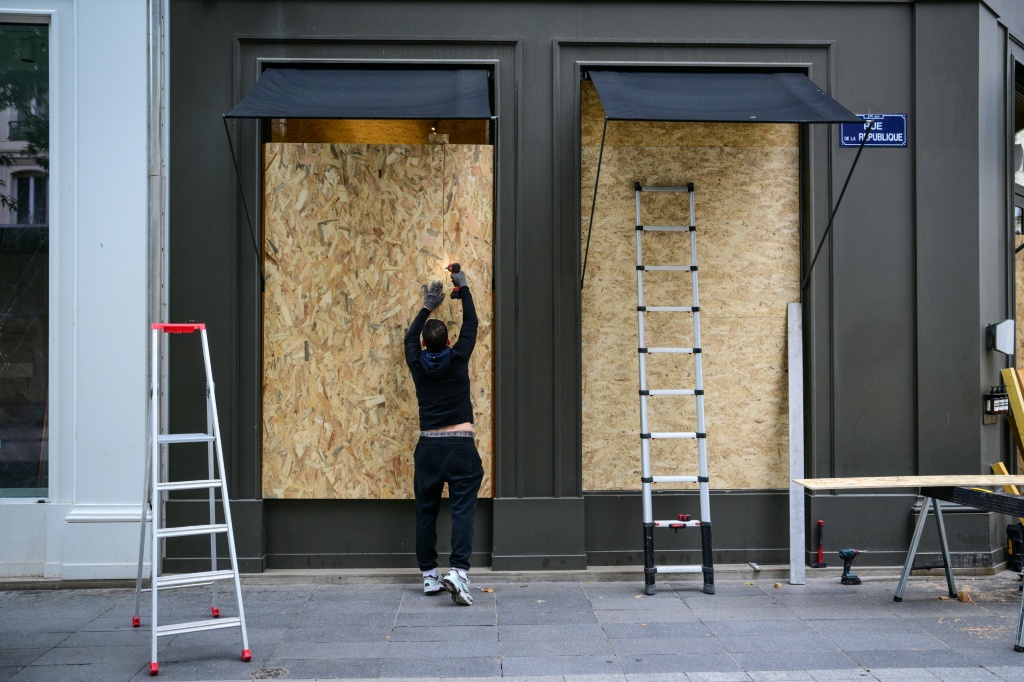A worker installs plywood boards on a shop window in Lyon ahead of protests — OLIVIER CHASSIGNOLE / AFP