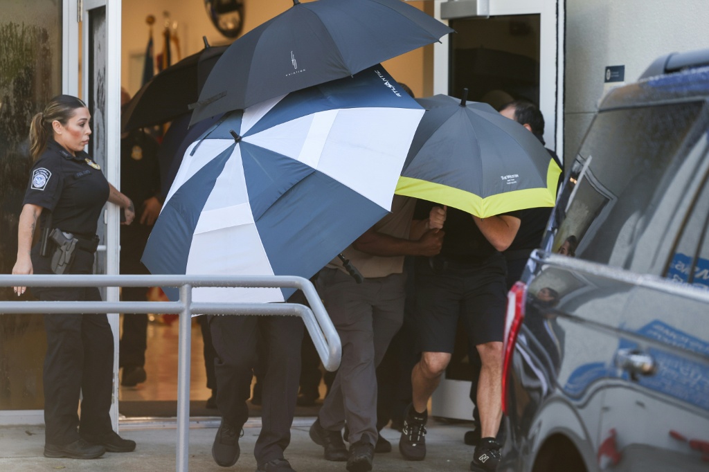 Flavio Bolsonaro and his family are shielded by umbrellas as they depart Opa Locka Executive Airport in Miami, Florida — Ricardo Arduengo / AFP