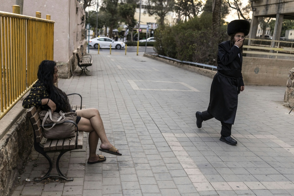 An ultra-Orthodox Jewish man walks past a woman sitting on a public bench in Arad on October 1, 2026. Ultra-Orthodox Jews are projected to account for roughly one-quarter of the Israeli population by mid-century. — JOHN WESSELS / AFP