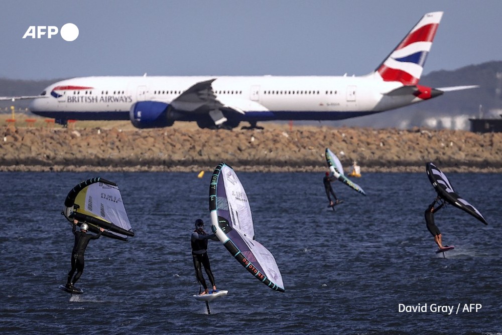 A group of wing surfers ride their boards in front of a British Airways plane preparing to take-off at Sydney International Airport on a windy spring day September 4, 2024.