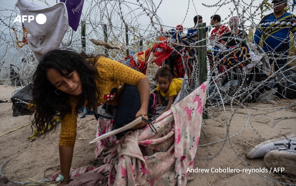 Migrants from Venezuela crawl through a hole in the razor wire