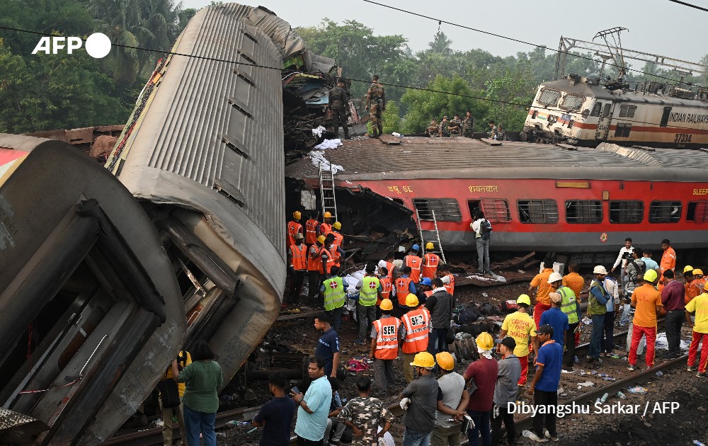 Rescue workers gather around damaged carriages at the accident site of a three-train collision near Balasore, Inida