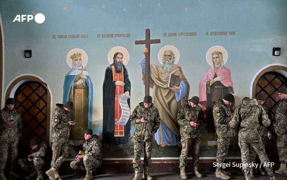 Ukrainian servicemen look their smartphones as they wait, shelting from the autumn rain as they stand next frescos in St. Michael's Cathedral in Kyiv