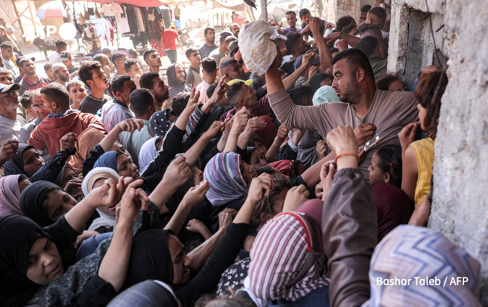 A man prepares to toss a bag of bread for another person as people crowd while queueing for bread outside a bakery in Khan Yunis in the southern Gaza Strip on October 23, 2024 