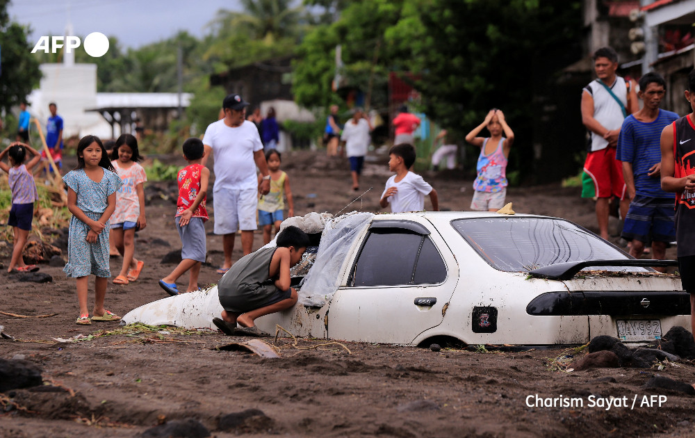 Residents look at a car buried by volcanic ash which cascaded into a village triggered by heavy rains brought about by Tropical Storm Trami at a village in Guinobatan town, Albay province South of Manila on October 23, 2024.