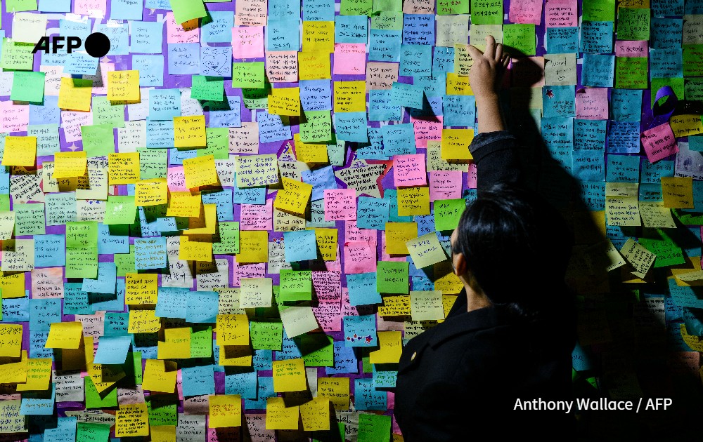 A person attaches a handwritten note next to others left on a board during a vigil in Seoul 