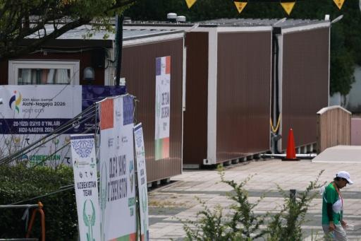 A man walks past temporary wooden container huts being used to house athletes for the 2026 Asian Games — DAVID GRAY / AFP