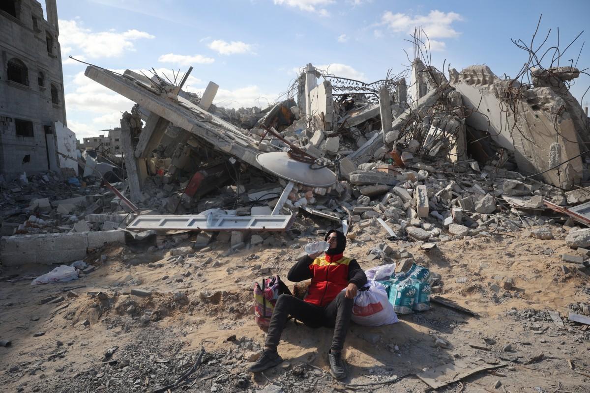 Un homme palestinien boit de l'eau en étant assis à côté de ses affaires près d'une maison détruite dans la ville de Rafah