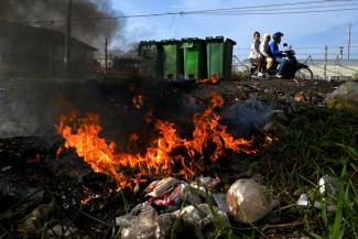 This photo shows people travelling on a motorbike past burning plastic waste on the outskirts of Phnom Penh