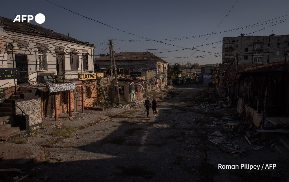 Local residents walk past damaged shops and buildings